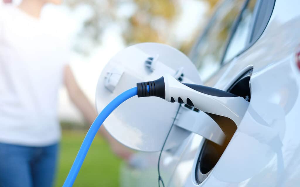 Voiture électrique blanche en cours de recharge avec un câble bleu et un pistolet de charge noir et blanc.