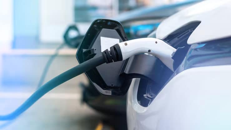 Recharge d'une voiture électrique blanche avec câble et pistolet de chargement branchés sur le port latéral.